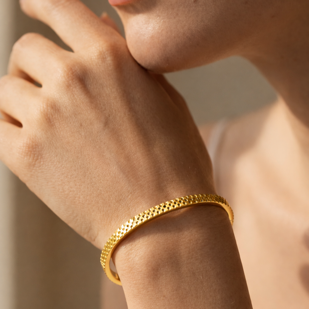 Pulsera rígida dorada tipo brazalete con borde dentado y corazones